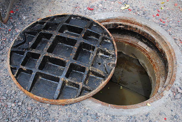 Partially open manhole on a street with watersewage visible below